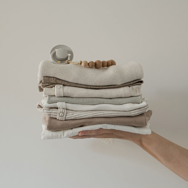 hand holding a bundle of folded baby clothes in neutral matching colours