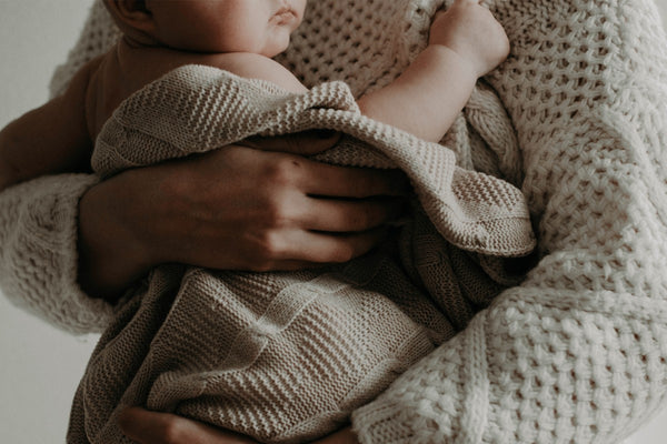 woman holding a baby wrapped in a wool blanket