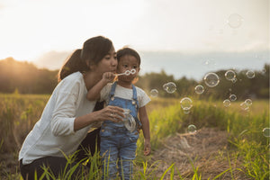 Asian woman and child blowing bubbles in a field